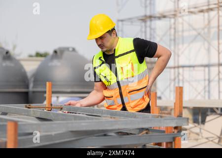 Il lavoratore edile in giubbotto di sicurezza e elmetto ispeziona la struttura in cantiere, avvertendo mal di schiena. Concetto di salute sul lavoro e. Foto Stock