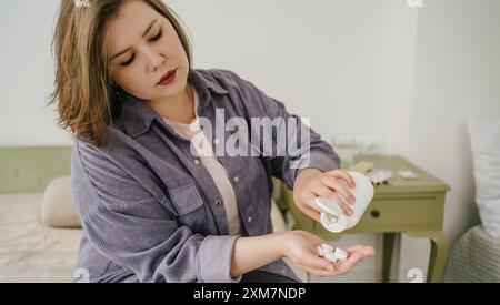 Donna che versa pillole bianche in mano dalla bottiglia. Plus size girl che prende pillole dietetiche, per perdere peso. Problemi delle persone con sottopeso e autoaccettazione. Foto Stock