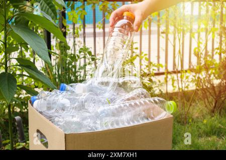 Tenere le mani e inserire i flaconi di plastica nella scatola marrone per rifiuti Foto Stock