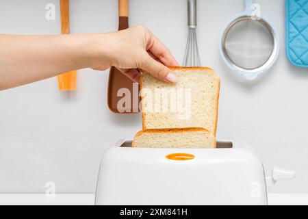 mano di donna che mette il pane nel tostapane. donna che fa un brindisi. tostare il pane in un tostapane. Foto Stock