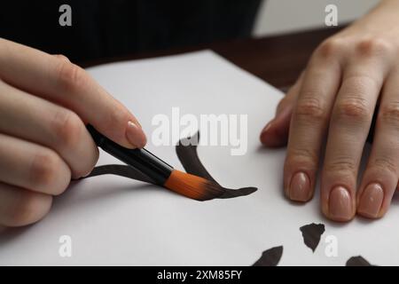 Calligrafia. Donna con la scritta a pennello ingresso in cinese su carta a tavola, primo piano Foto Stock