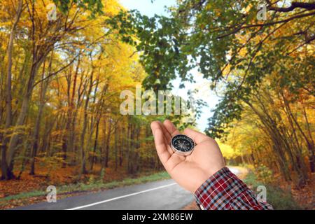 Uomo che tiene la bussola vicino alla strada che attraversa la foresta in autunno, primo piano Foto Stock