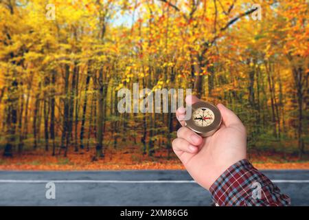 Uomo che tiene la bussola vicino alla strada che attraversa la foresta in autunno, primo piano Foto Stock