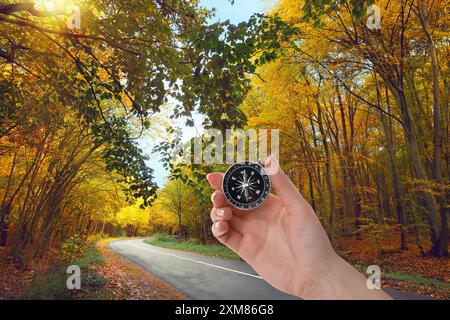 Donna che tiene la bussola vicino alla strada che attraversa la foresta in autunno, primo piano Foto Stock