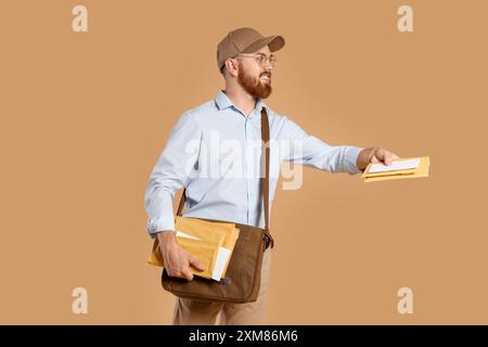 Felice giovane postino con borsa in pelle che consegna lettere su sfondo marrone Foto Stock