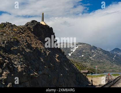 I binari attraversano il confine tra Stati Uniti e Canada, segnato dal piccolo obelisco in alto a sinistra, in cima al White Pass vicino a Skagway, Alaska Foto Stock