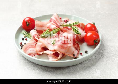 Fette di pancetta cruda, spezie e pomodori su un tavolo grigio chiaro Foto Stock
