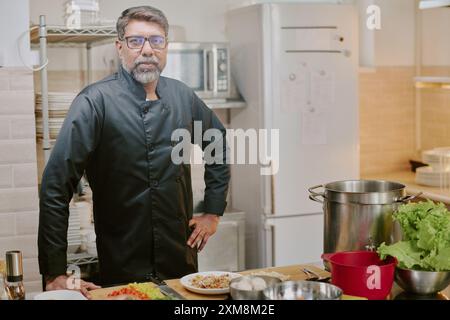 Chef indiano di mezza età con barba grigia che guarda direttamente alla fotocamera mostrando la sua serietà e la sua esperienza sul viso mentre posa per un ritratto Foto Stock