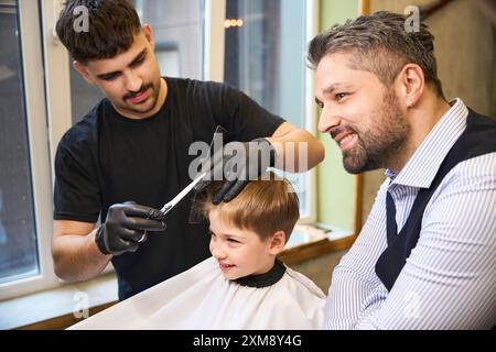 Padre che guarda il barbiere che fa il taglio di capelli di precisione al suo bambino Foto Stock