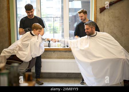 Bambino che dà il pugno al padre che siede sulla sedia da barbiere Foto Stock