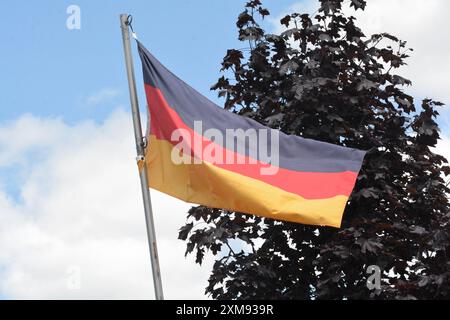 La bandiera nazionale della Germania vola su un palo in una splendida giornata estiva con uno sfondo di cielo blu e nuvole bianche. Foto Stock