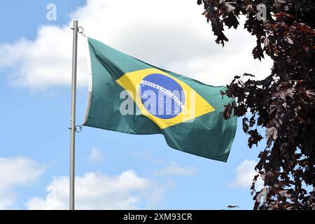 La bandiera nazionale del Brasile vola su un palo in una splendida giornata estiva con uno sfondo di cielo blu e nuvole bianche. Foto Stock