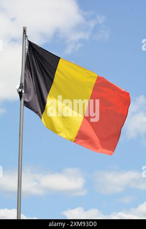 La bandiera nazionale del Belgio vola su un palo in una splendida giornata estiva con uno sfondo di cielo blu e nuvole bianche. Foto Stock