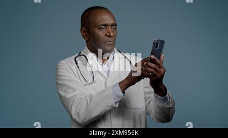 Uomo afroamericano maschio medico in uniforme bianca digitando risposta invio messaggio e-mail su smartphone navigazione scheda paziente utilizzando medico virtuale Foto Stock