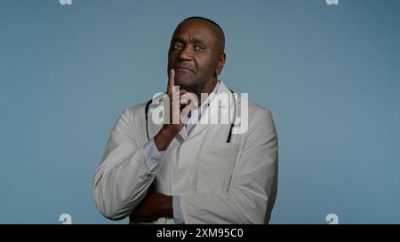 Pensivo premuroso uomo afroamericano medico medico professionista maschio operatore sanitario indossare cappotto medico bianco in sfondo blu idea Ponder Foto Stock