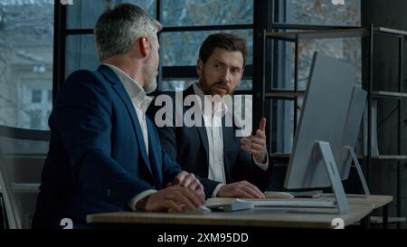 Due uomini caucasici uomini d'affari professionisti lavorano insieme utilizzando un computer in ufficio discutendo di progetti aziendali controllo finanziario piano dati colleghi Foto Stock