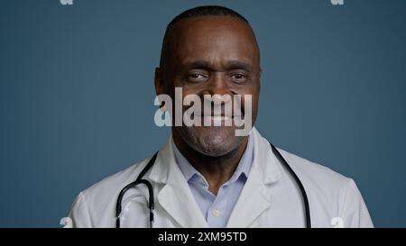 Primo piano sorridente uomo afroamericano medico in posa in studio sfondo blu etnico maschio professionale medico dipendente chirurgo terapeuta dentista Foto Stock