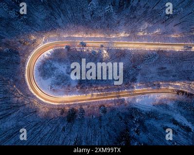 Fari per auto che illuminano una strada tortuosa d'inverno dopo il tramonto. Tempo di esposizione prolungato. Trasporto notturno in inverno. Foto Stock