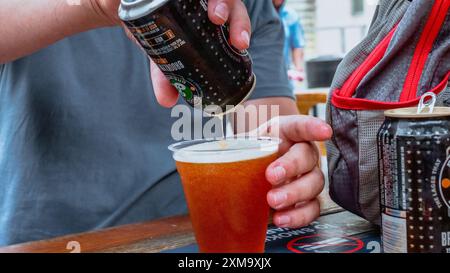 Birra versata in una tazza di plastica su un tavolo di legno all'aperto al bar con sfondo sfocato. New York NY USA 2023-07-30 Foto Stock