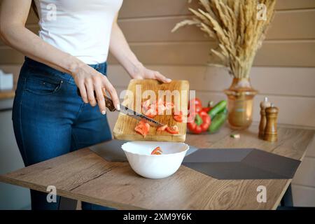 Vista ravvicinata di una donna irriconoscibile che versa il pomodoro tritato in una ciotola dal tagliere di legno Foto Stock