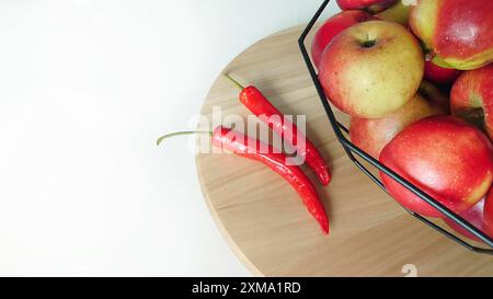 Un cestino di mele con due peperoncini su una superficie di legno, evidenziando colori contrastanti Foto Stock