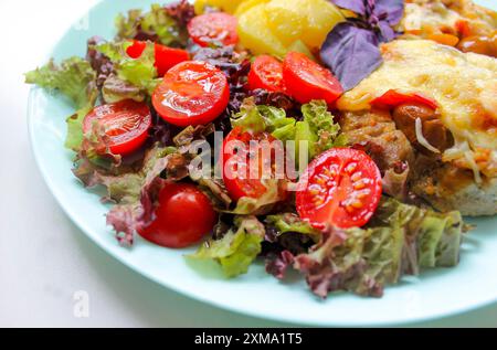 Un piatto con insalata fresca con pomodori ciliegini, lattuga, basilico e un contorno di piatto coperto di formaggio Foto Stock