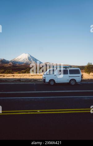 Pulmino bianco su strada di fronte a montagne innevate e cielo blu, Parco Nazionale del Tongariro, nuova Zelanda Foto Stock