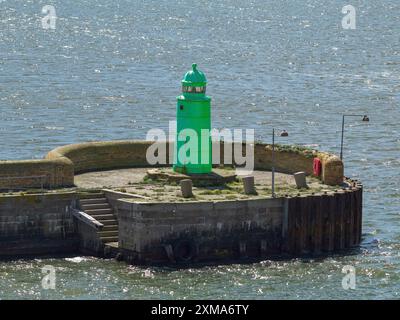 Un piccolo faro verde su un molo con un muro di pietra nel mezzo dell'acqua di mare ondulata, esbjerg, danimarca Foto Stock