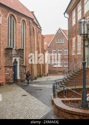 Un anziano cammina davanti a edifici in mattoni e vecchie lanterne lungo una stretta strada acciottolata, stade, germania Foto Stock