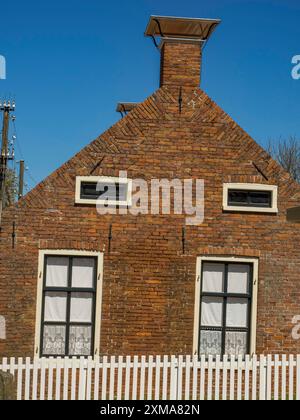 Una vecchia casa in mattoni con finestre bianche e un camino dietro una recinzione bianca, enkhuizen, paesi bassi Foto Stock