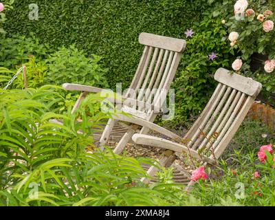 Due sdraio in legno in un giardino verde, circondato da fiori fioriti e vegetazione lussureggiante, borken, vestfalia, germania Foto Stock