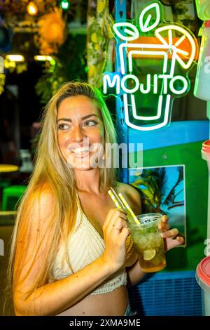 Foto verticale di una donna felice sorridente mentre beve un cocktail mojito in un bar godendosi la notte d'estate Foto Stock