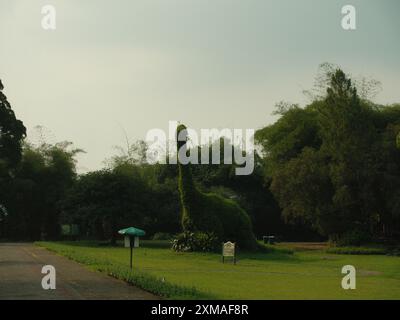 Una grande statua di dinosauro si trova in un parco con un cartello verde nelle vicinanze. La scena è tranquilla e serena, con la statua e il cartello che si fondono con la natura Foto Stock