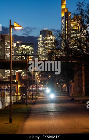 Skyline del centro di Francoforte sul meno, ciclista con luce sulla pista ciclabile, marciapiede, passeggiata lungo il fiume meno, crepuscolo, Assia, Germania Foto Stock