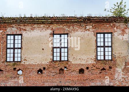 Un edificio abbandonato in mattoni antichi con finestre rotte. Le pareti mostrano segni di usura e invecchiamento, rivelando la sua angoscia Foto Stock