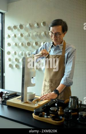 Barista senior esperto che prepara il caffè per i clienti utilizzando una moderna macchina da caffè Foto Stock