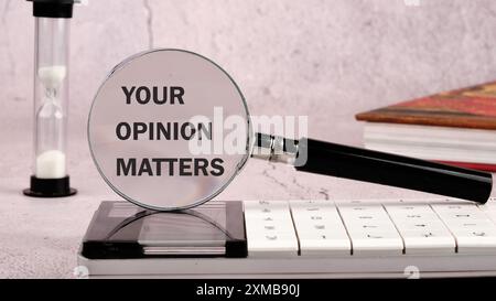 Un cartello di testo che mostra LA TUA OPINIONE È IMPORTANTE attraverso una lente di ingrandimento su una parete grigia, vista frontale Foto Stock