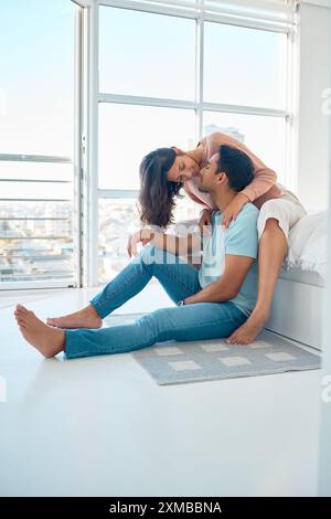 Coppia, baci e sorridi in camera da letto, mattina e amore sul letto con legame, cura e romanticismo a casa. Uomo, donna e contatto con la felicità, le vacanze o.. Foto Stock