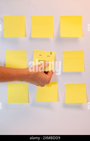 Una mano regge una nota adesiva gialla con una faccia sorridente. Le due note sono posizionate l'una accanto all'altra Foto Stock