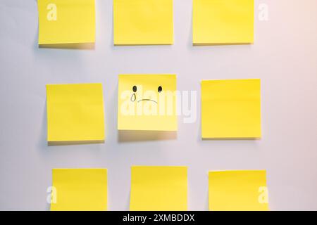 Un pezzo di carta giallo con una faccia triste disegnata su di esso è circondato da altri pezzi di carta gialli Foto Stock