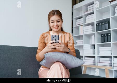 la donna si rilassa su un divano, scorrendo i social media sul suo smartphone. Foto Stock