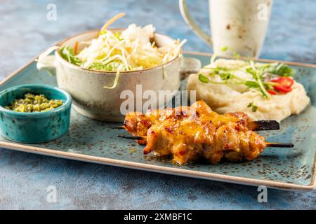 kebab di pollo con purè di patate, insalata e salsa al pesto. Il ristorante serve un piatto blu Foto Stock