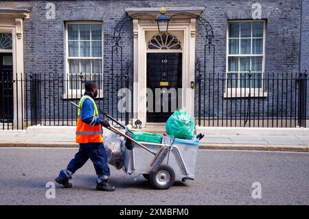 Un collezionista di rifiuti cammina davanti alla porta del numero 10 di Downing Street. La casa del nuovo primo Ministro, Sir Keir Starmer. Foto Stock