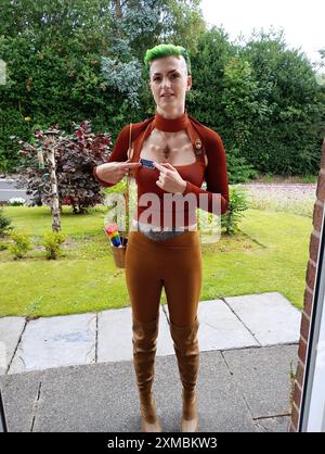 Giovane donna vestita per il convegno scfi con capelli verdi, modifiche del corpo sulla testa, clavicola e che punta al badge emotivo dell'agente di sicurezza. Foto Stock