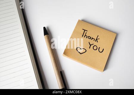 Nota adesiva con frase scritta a mano ringraziamento su sfondo bianco con penna e quaderno Foto Stock