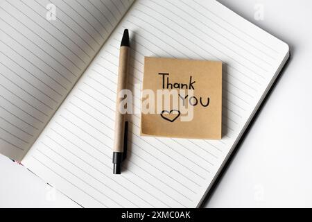 Nota adesiva con frase scritta a mano ringraziamento su un notebook con vista dall'alto della penna Foto Stock