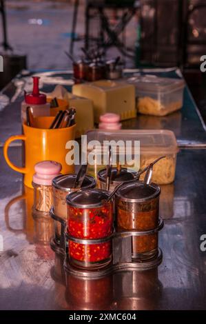 Condimenti e spezie su un tavolo all'aperto del ristorante locale, inclusa salsa al peperoncino, al mercato russo, Phnom Penh, Cambogia. Credito: Kraig Lieb Foto Stock