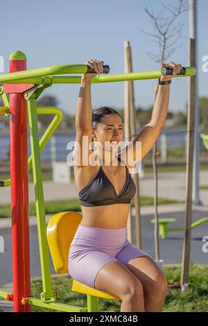 Ragazza latina su una macchina per esercizi in un parco pubblico. Foto Stock