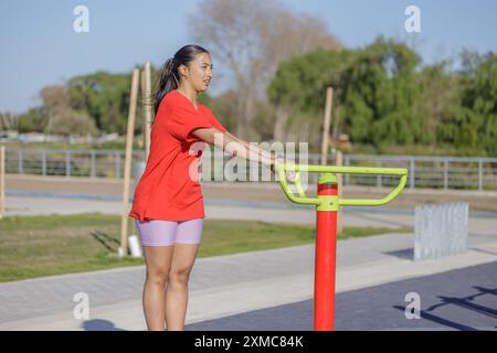 Ragazza latina su una macchina per esercizi in un parco pubblico. Foto Stock