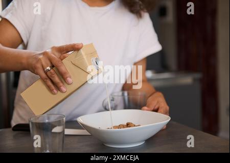 Persona che versa il latte di una scatola in un recipiente di cereali in cucina. Un ambiente informale e accogliente per la colazione cattura l'attenzione del pubblico. Foto Stock